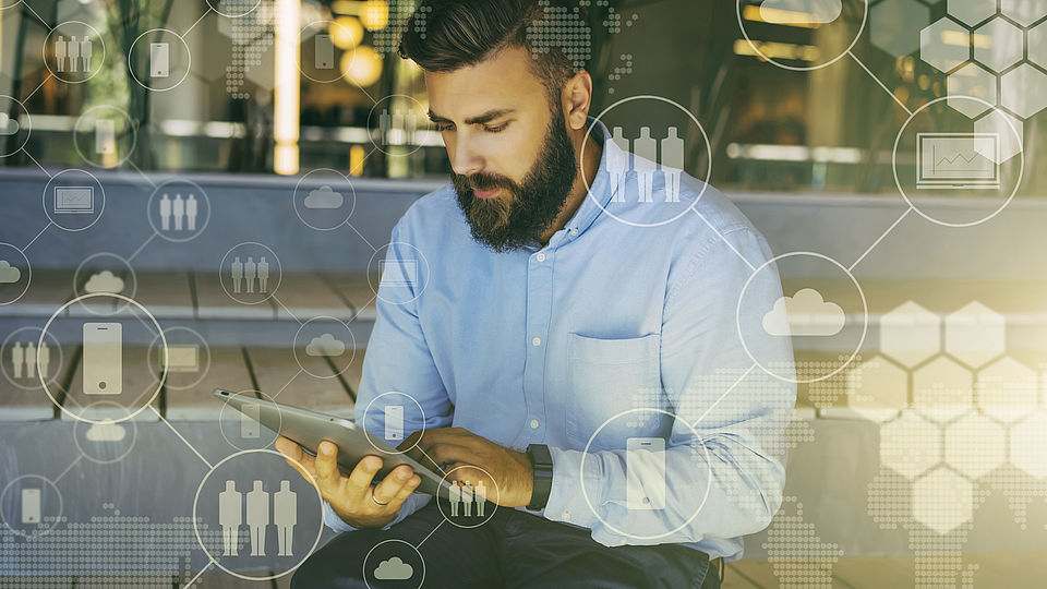 Ein Mann sitzt mit einem Tablet auf einer Bank. Um ihn herum wird symbolisch die digitale Welt dargestellt. 
